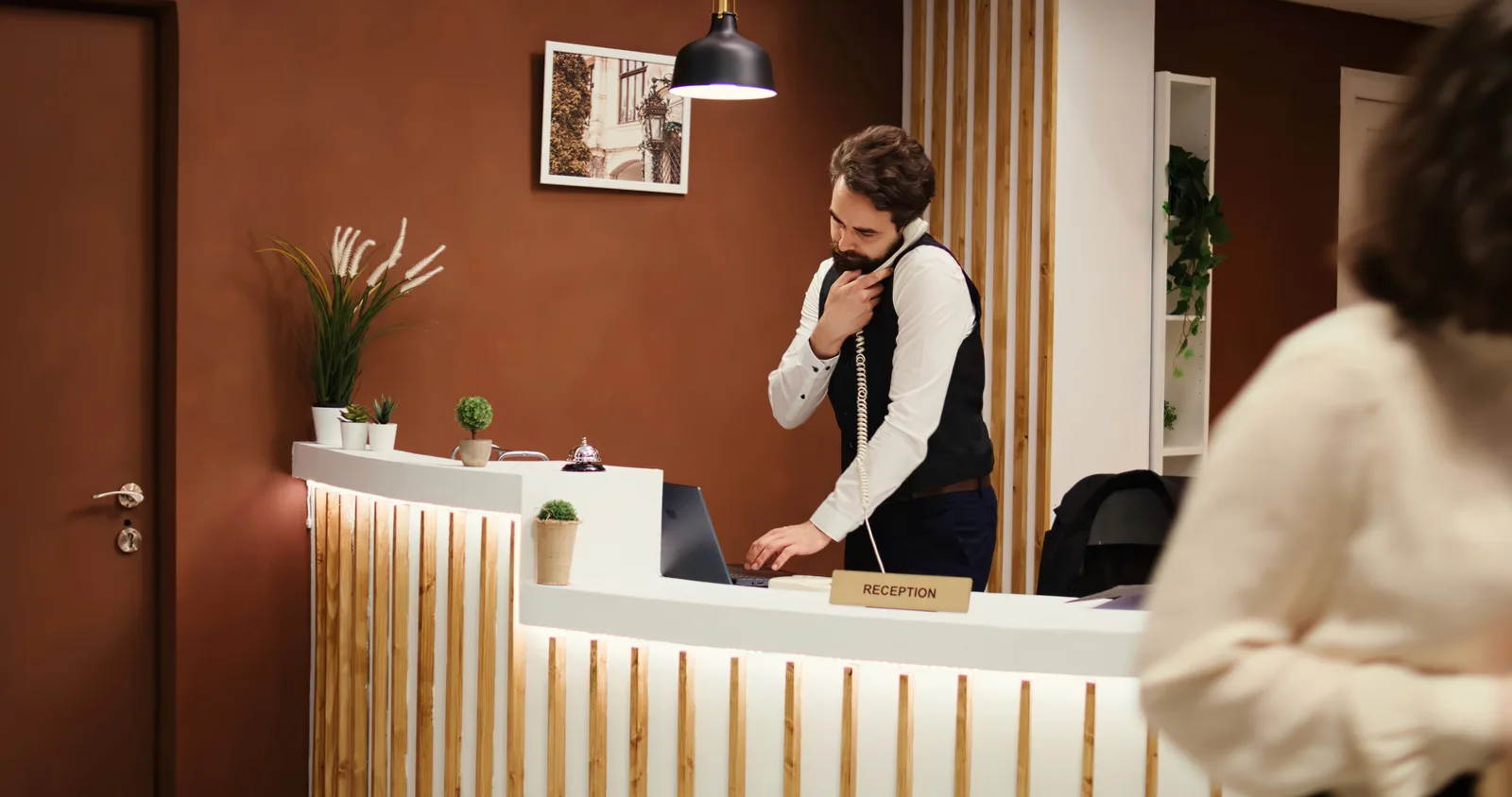 Recepcionista d'un hotel boutique independent atenent un hoste al taulell